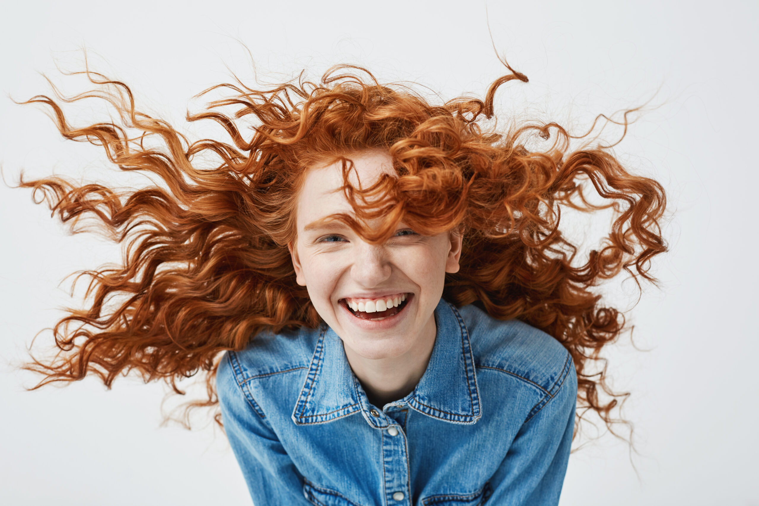 Portrait of beautiful cheerful redhead girl with flying curly hair smiling laughing looking at camera over white background.