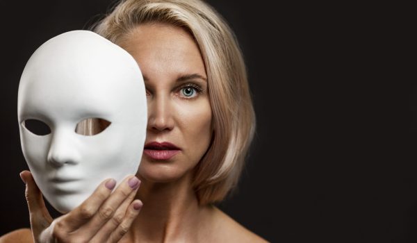 Blonde woman with a white mask in her hand. Close-up. Black back