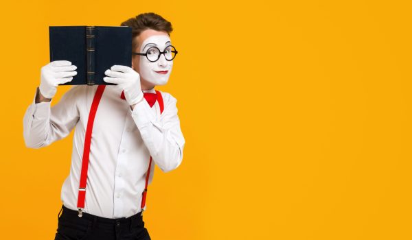 portrait of mime man artist reading book isolated on yellow background. copy space for text