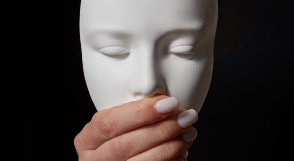 Woman fingers close mouth of gypsum mask face on a black background, copy space. Speak no evil. Concept three wise monkeys